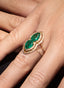 Close-up of emerald and diamond ring on model's hand, showcasing fine craftsmanship.