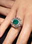 Close-up of emerald and diamond ring on model's hand, showcasing fine craftsmanship.