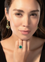 Close-up of emerald and diamond ring on model's hand, showcasing fine craftsmanship.