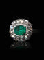 Close-up of emerald and diamond ring with a black background, highlighting gemstone brilliance.